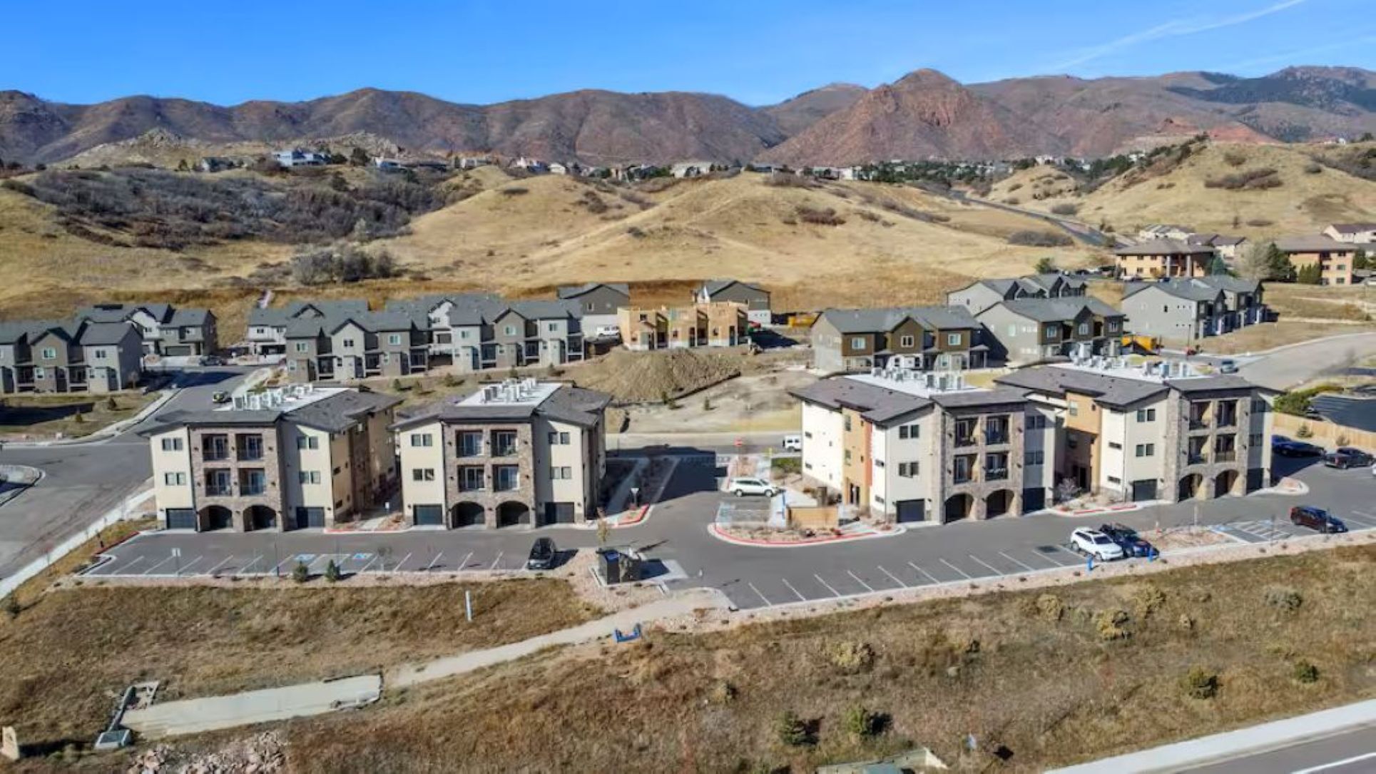 Zona residencial con edificios modernos de varios pisos, un estacionamiento y montañas al fondo.