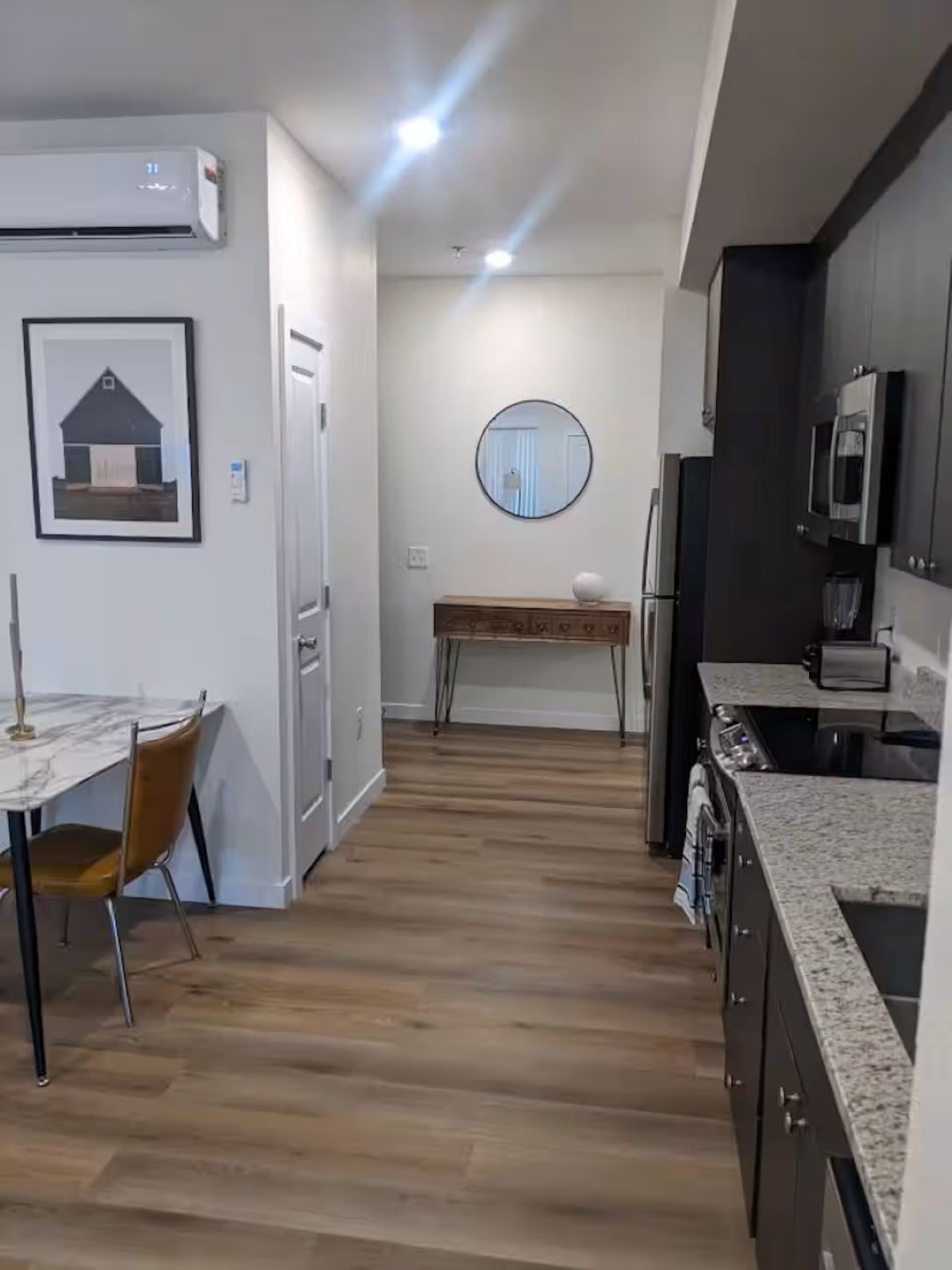 A compact kitchen with a dining area, a round mirror, and a framed picture on the wall.