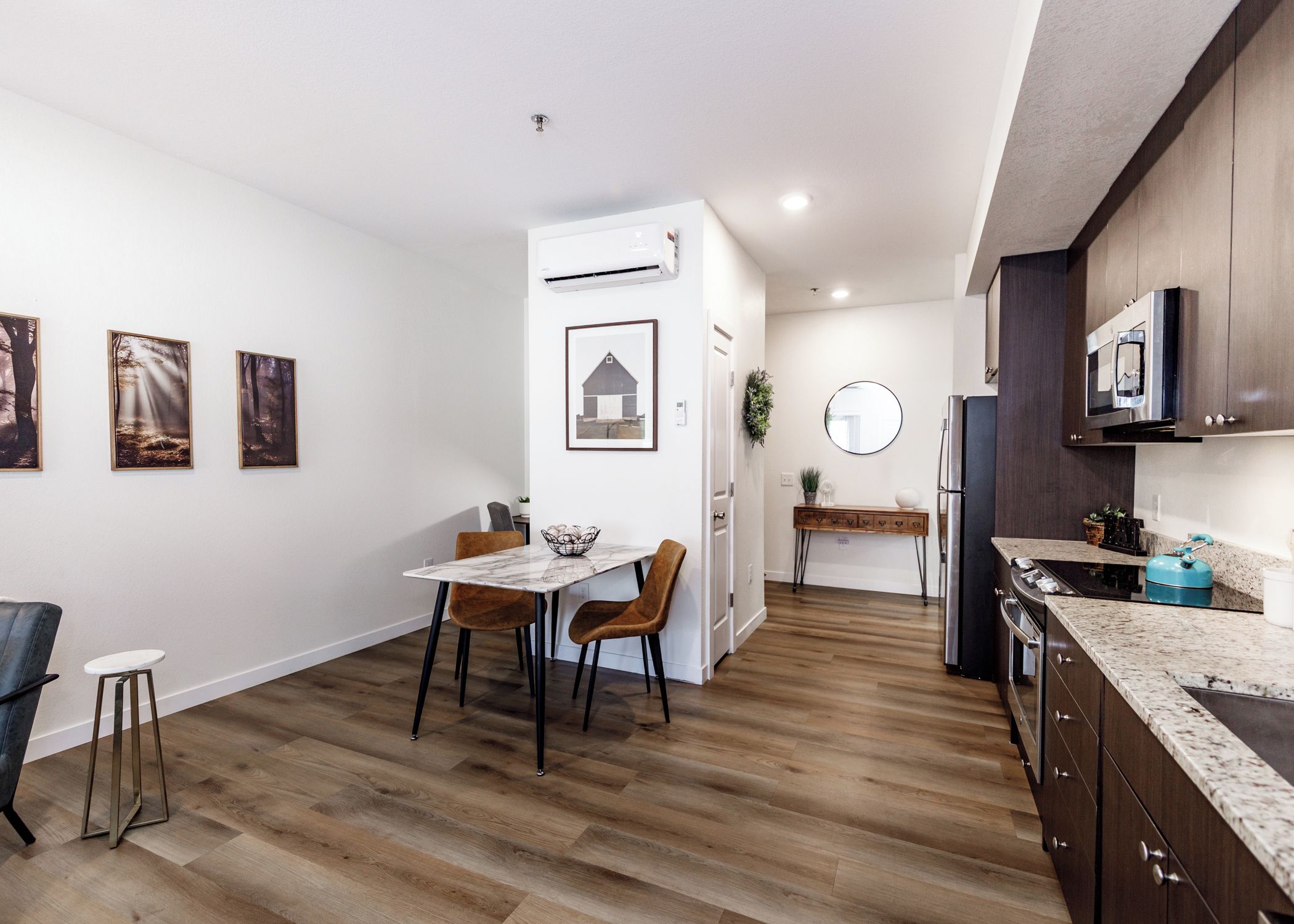 A modern kitchen with wooden flooring, a dining area with a marble table, and a kitchen island.