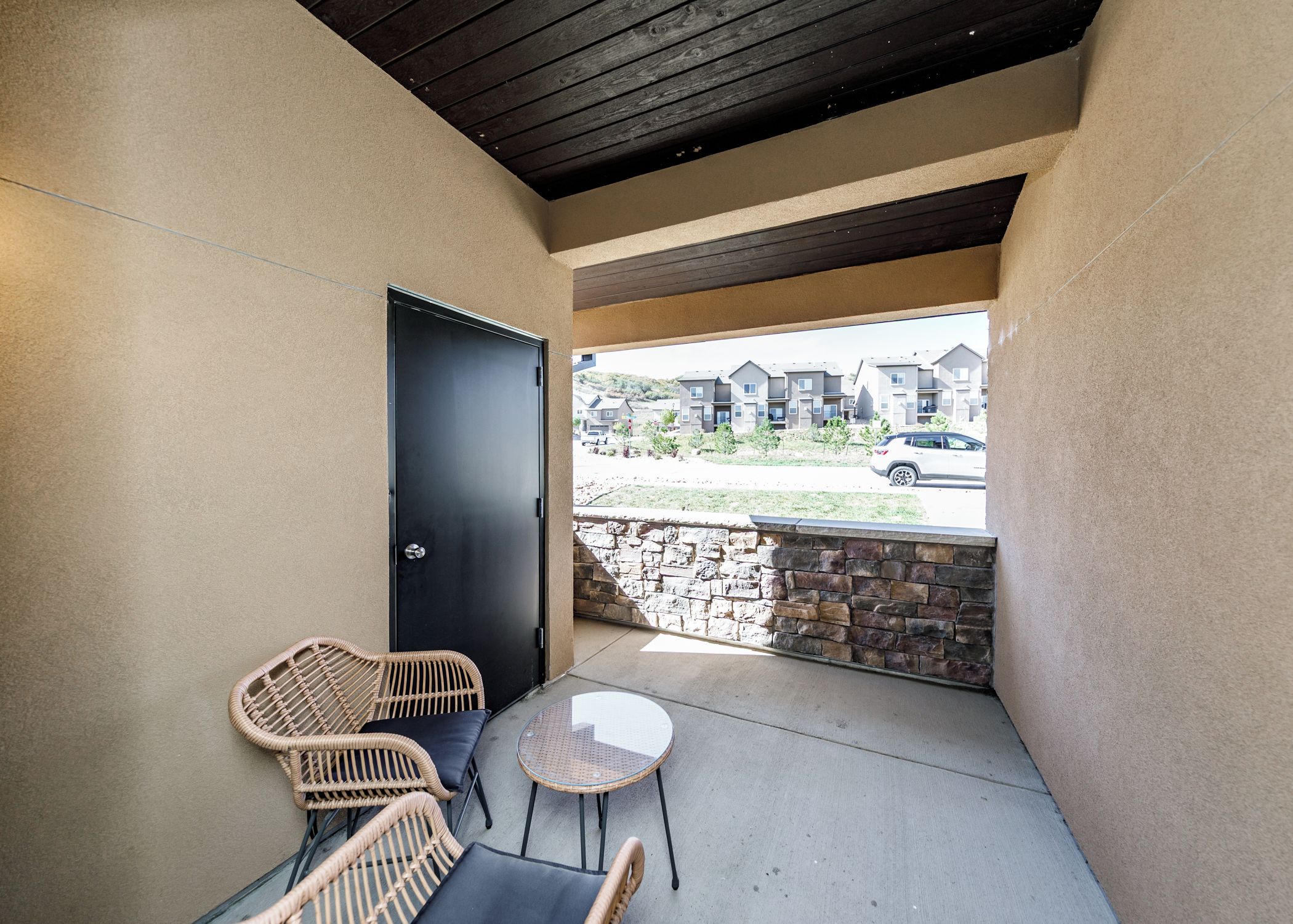 Een overdekt terras met een stenen muur, een deur en uitzicht op een wooncomplex.