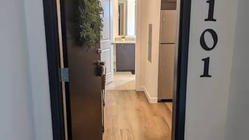 A hallway with a wooden floor, a welcome mat, a door, and a wall-mounted sign with the number 101.