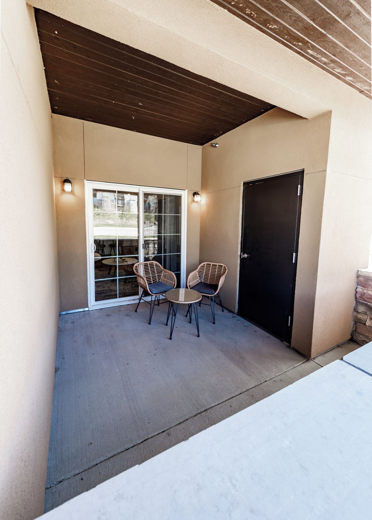Un patio al aire libre con zona de estar cubierta, puerta corredera de vidrio y una puerta negra.