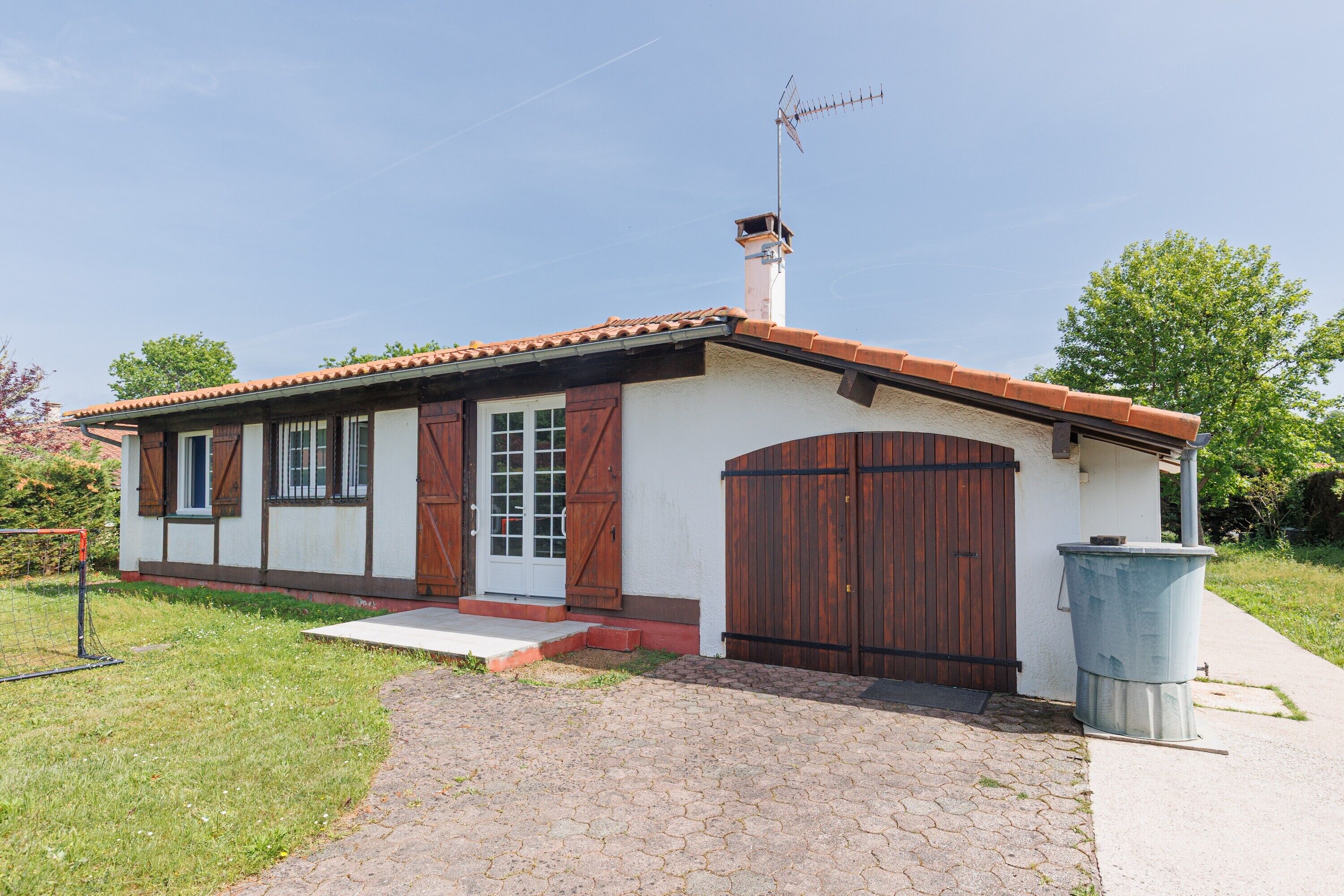 A small building with a tiled roof, a chimney, a wooden door, and a trash bin.