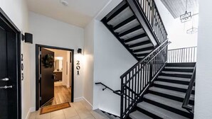 Un escalier avec une rampe noire et une porte portant l’inscription « 201 », qui donne accès à une pièce.