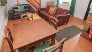 Ein Wohnzimmer mit Holztisch und -stühlen, zwei Ledersofas, einer Holztreppe und einem Fenster mit Vorhängen.