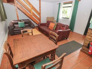 A living room with a wooden table and chairs, two leather sofas, a wooden staircase, and a window with curtains. - Cabin No. 9 - Salt and Fern Cabins (Port Talbot)