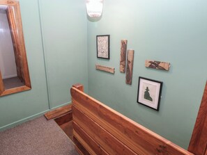A hallway with a wooden bench, a mirror, and wall-mounted artwork including a framed picture and wooden plaques. - Cabin No. 9 - Salt and Fern Cabins (Port Talbot)