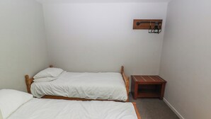 Eine kleine, einfache Unterkunft mit zwei Einzelbetten, einem Holznachttisch und einem an der Wand befestigten Regal.