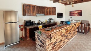 A kitchen with a central island, wooden cabinets, a stainless steel refrigerator, and a flat-screen TV on the wall. - Villa Ryad Ibou (Aguerd)