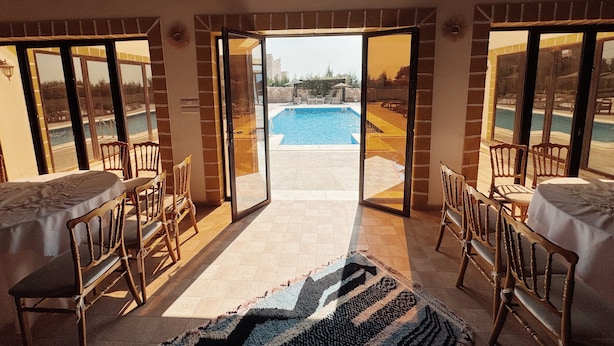 An open-plan room with a pool view, wooden furniture, and a patterned rug. - Villa Ryad Ibou (Aguerd)