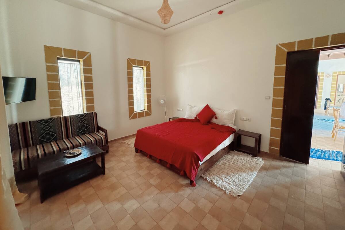 Quarto com cama, sofá, televisão e ventilador.