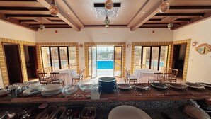 A dining area with tables set for meals, a pool view, and a kitchen area with utensils. - Villa Ryad Ibou (Aguerd)
