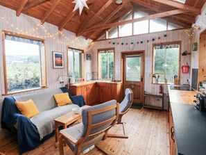 A cozy cabin interior with a wooden ceiling, a sofa with cushions, a dining table, a kitchen area, and large windows. - Cosy Eco Cabin (Newport)