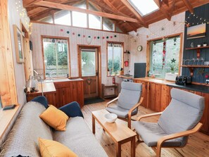 Ein gemütliches Blockhaus-Interieur mit Holzwänden, einer Couch, zwei Sesseln, einem kleinen Tisch und einer Küchenzeile mit einem Toaster.