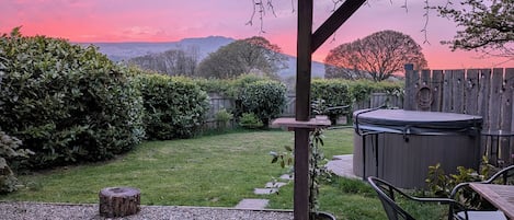 A patio with a hot tub, wooden deck, and a view of a mountain range.