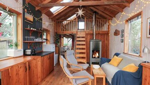 A cozy cabin interior with a loft bedroom, a dining area, and a kitchen. - Cosy Eco Cabin (Newport)