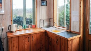 A wooden cabin kitchen with a sink, window, and string lights. - Cosy Eco Cabin (Newport)