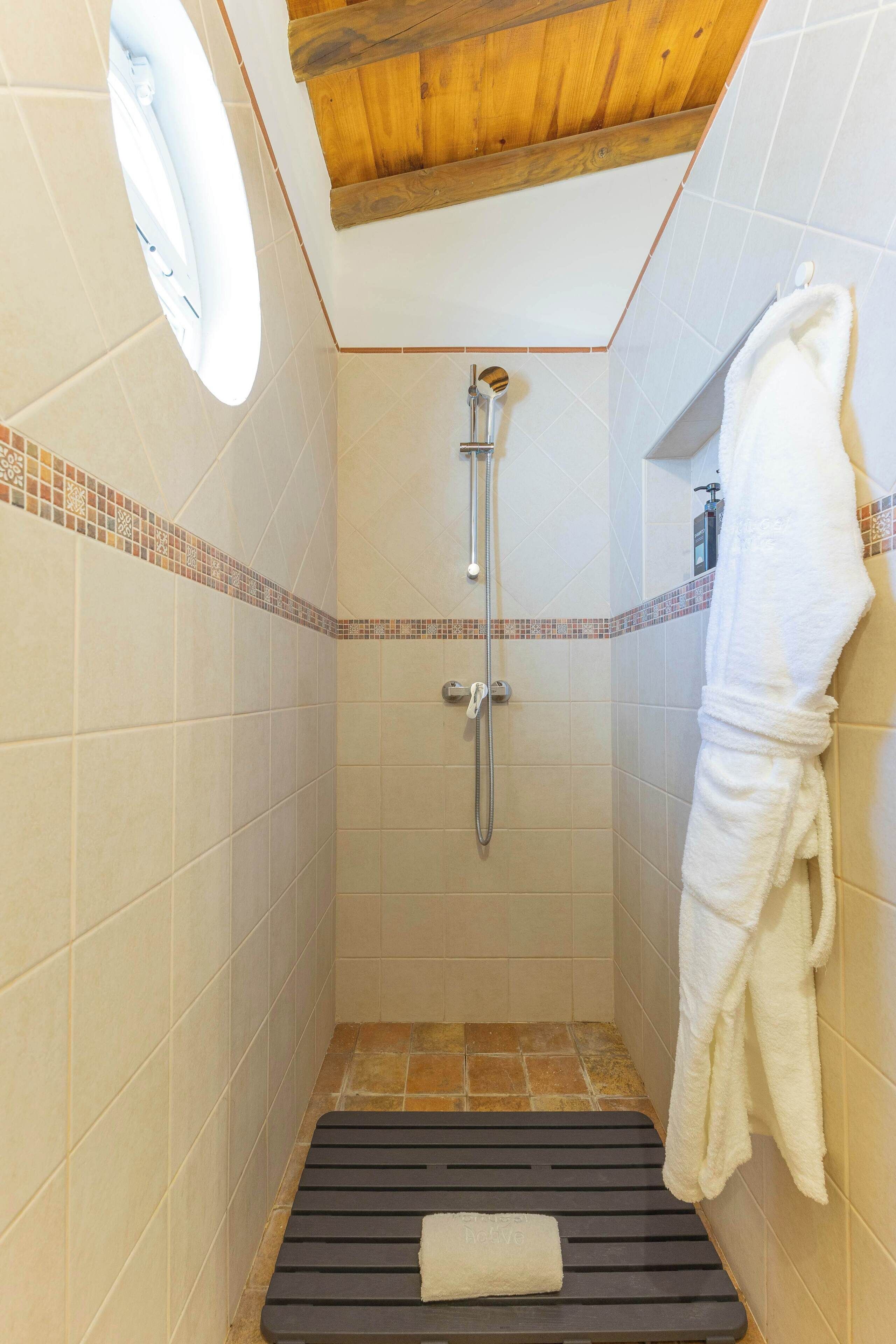 Eine Dusche mit Duschhandstück, ein Handtuch am Boden und ein Handtuch an der Wand.