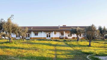 A two-story building with a tiled roof, surrounded by a grassy field and trees.