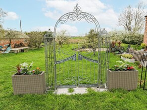 A wrought iron gate with a decorative arch, surrounded by a well-maintained lawn and potted plants. - The Retreat (Goole)