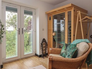 A room with a sliding glass door, a wicker sofa, a wooden cabinet, and a hanging coat rack. - The Retreat (Goole)