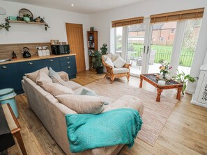 A living room with a sofa, a coffee table, a chair, a bookshelf, and a kitchen area with a microwave. - The Retreat (Goole)