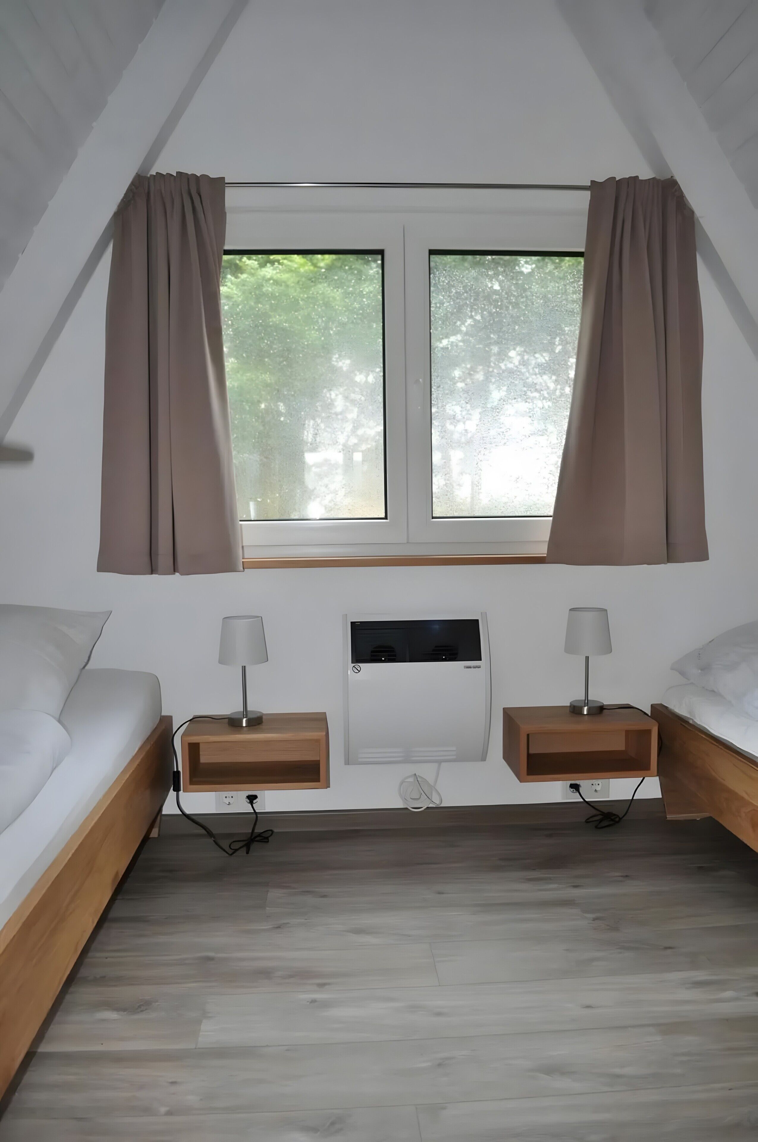 Una habitación con techo inclinado, dos camas, una ventana con cortinas, un equipo de aire acondicionado y lámparas de noche.