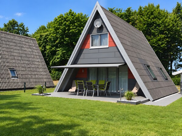 A modern house with a triangular roof, a balcony with chairs, and a small window.