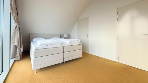 A bedroom with a bed, a wardrobe, a window with curtains, and a lamp. - Luxury Beachfront Apartment for 5 (Egmond aan Zee)