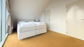 Ein Schlafzimmer mit Bett, Kleiderschrank, einem Fenster mit Vorhängen und einer Lampe.