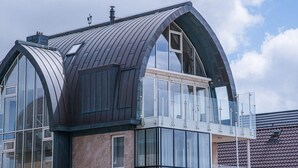 A modern building with a curved roof, large windows, and a balcony with glass railings. - Luxury Beachfront Apartment for 5 (Egmond aan Zee)