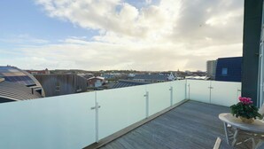 A rooftop terrace with a view of surrounding buildings, a table with a potted plant, and a railing. - Luxury Beachfront Apartment for 5 (Egmond aan Zee)