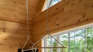Un intérieur en bois avec un fauteuil suspendu, un téléviseur et une grande fenêtre donnant sur une forêt.