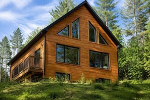 A wooden cabin with large windows, a balcony, and a forested backdrop.