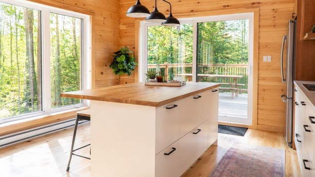 Une cuisine rustique, aménagée dans une cabane en bois, avec un grand îlot central, des portes doubles et une vue sur la forêt.