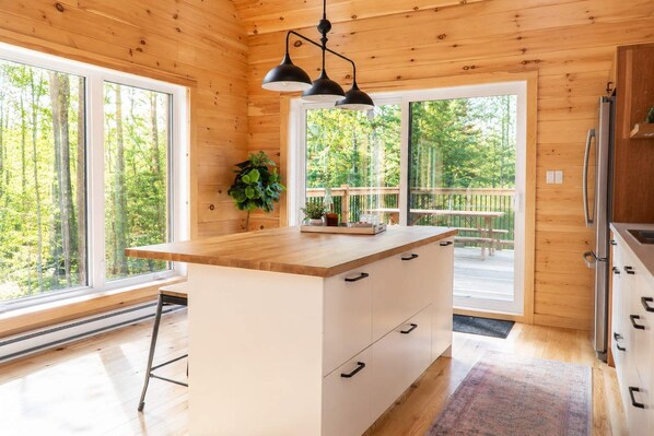A wooden cabin kitchen with a large island, double doors, and a view of the forest.