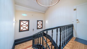A staircase with wooden steps and black balusters, a white door with a gold handle, and a ceiling light fixture. - Mercadores Apartment by Amber Star Rent (Porto)