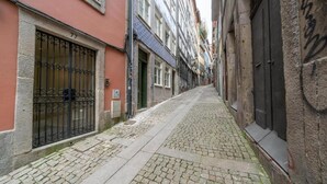 A narrow cobblestone street flanked by buildings with metal gates and a stone wall. - Mercadores Apartment by Amber Star Rent (Porto)
