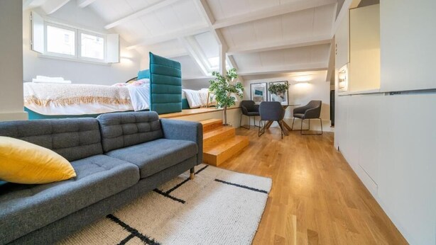 A modern loft-style room with a gray sofa, a teal accent wall, wooden flooring, and a staircase leading to an upper level. - Mercadores Apartment by Amber Star Rent (Porto)