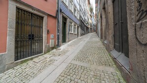 A narrow cobblestone street flanked by buildings with barred windows and doors. - Mercadores Apartment by Amber Star Rent (Porto)