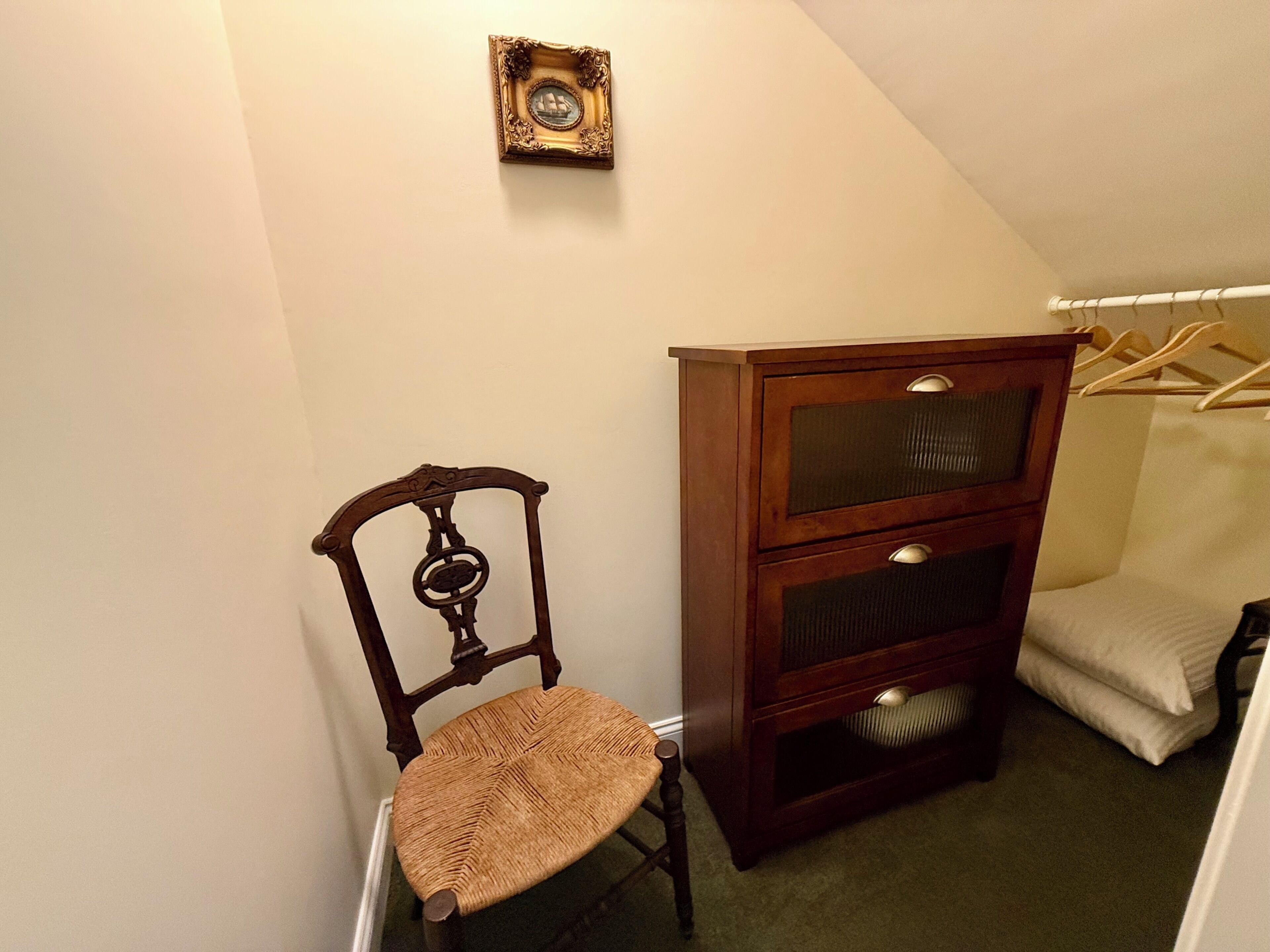 Ein Eckzimmer mit einem Holzbett, einer Kommode mit Schubladen und einem Kleiderhaken.