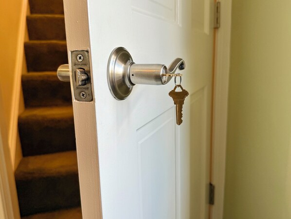 A door with a keyhole and a lock, a stairway to the left, and a white door frame.
