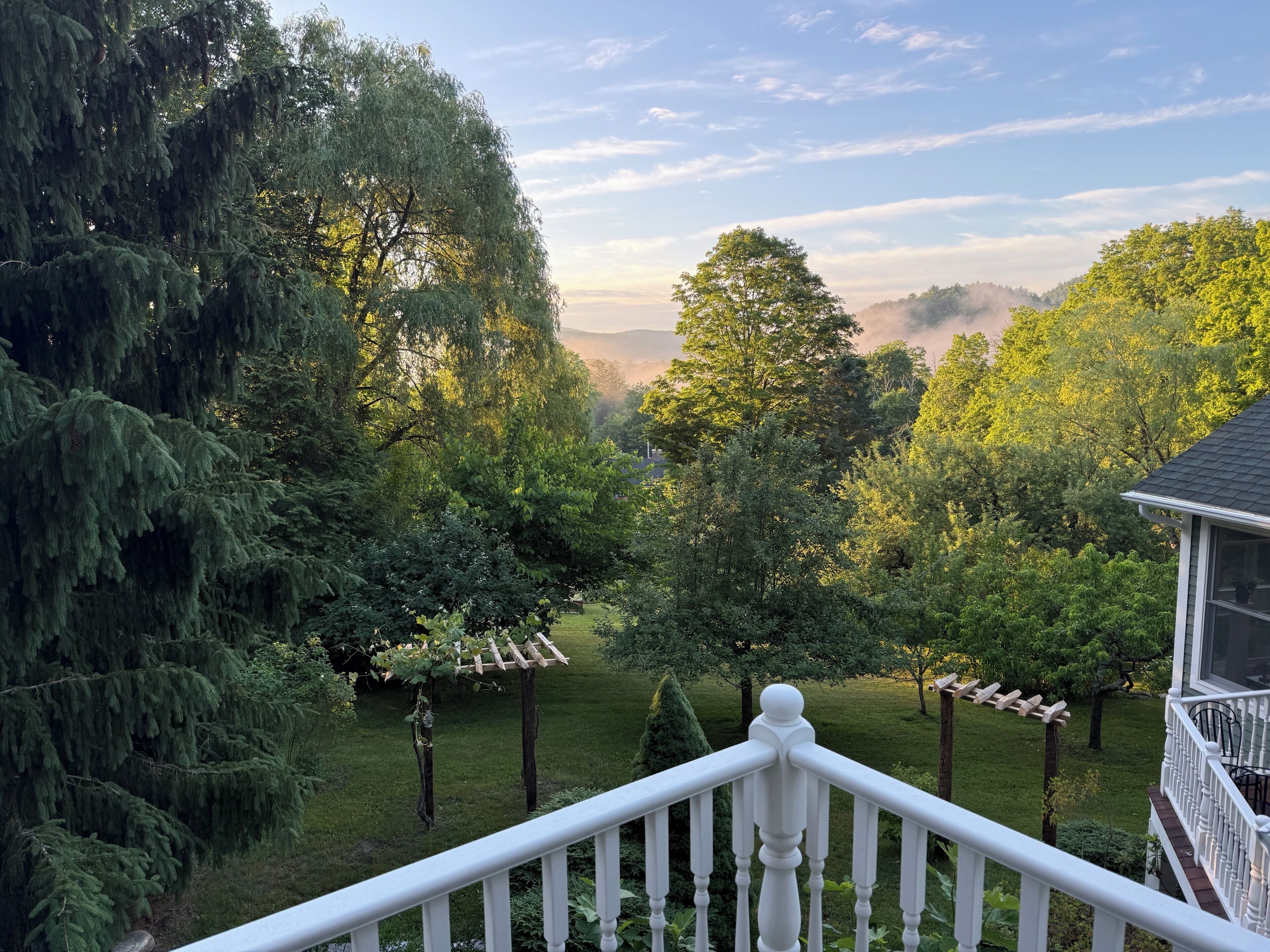 Propiedad residencial con vistas a un jardín exuberante, una pérgola de madera y una barandilla blanca.