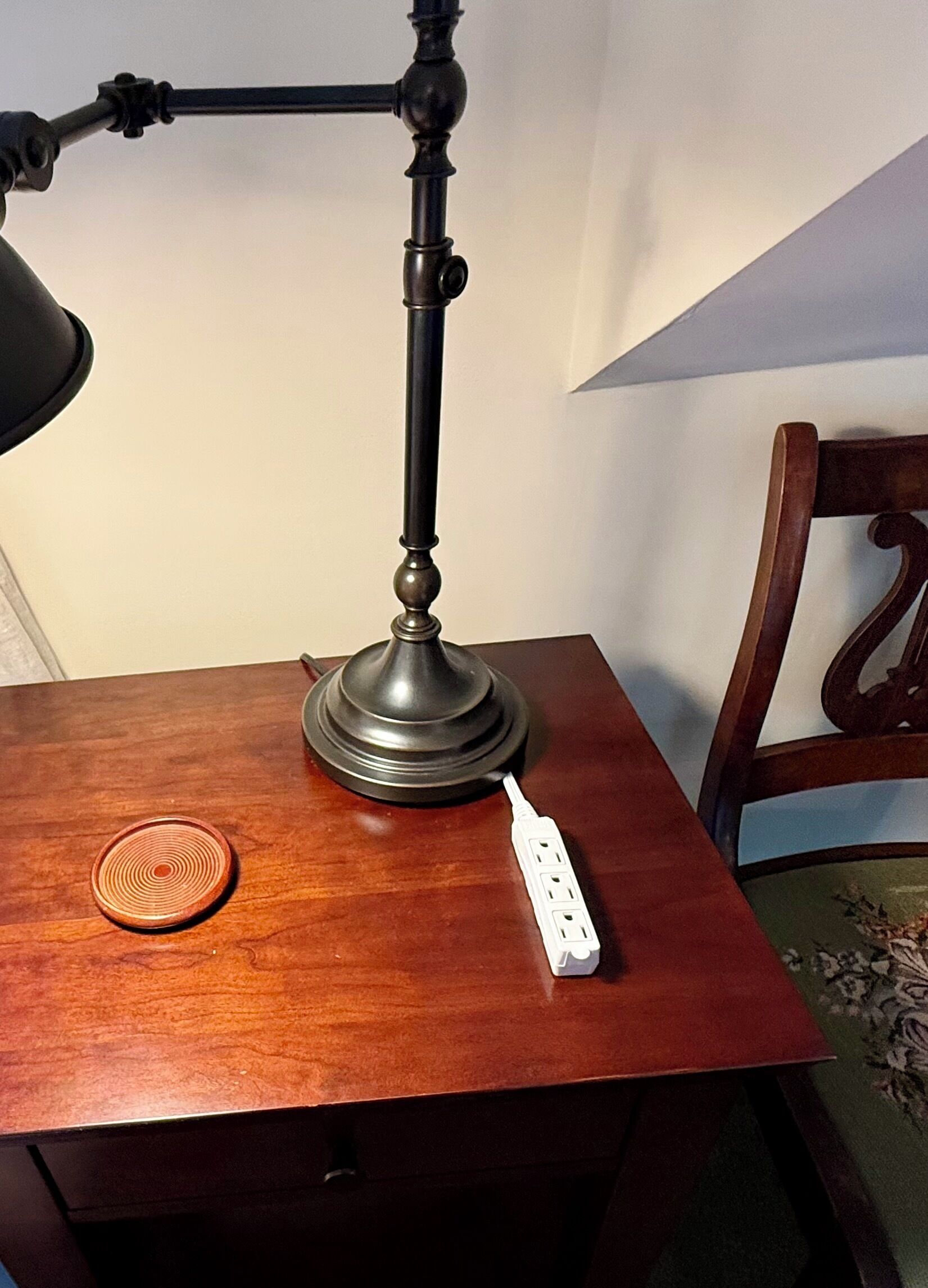 Een houten tafel met een bureaulamp, een stekkerdoos en een onderzetter.