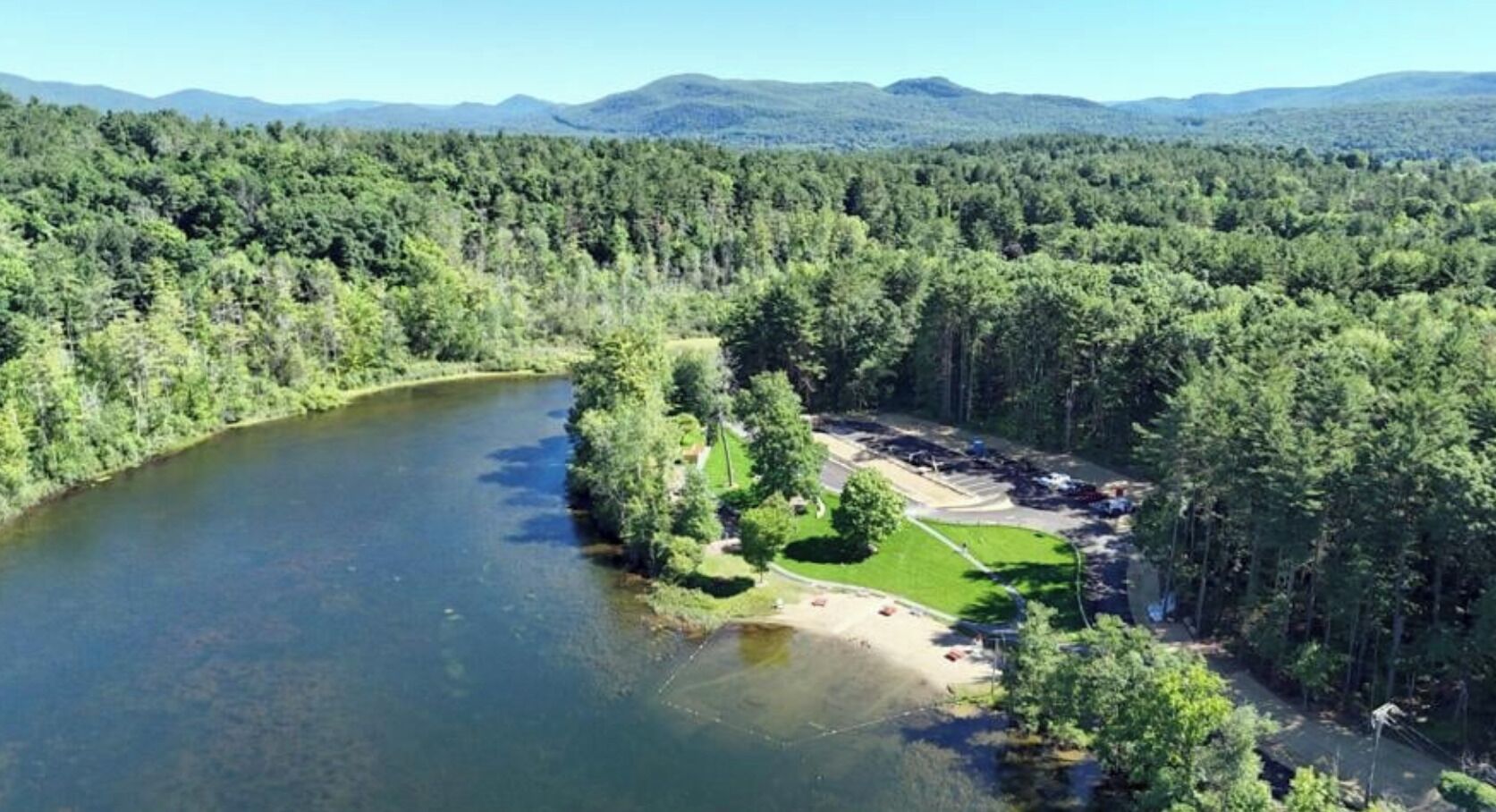 Un fiume circondato da una fitta foresta, un'area di parcheggio e un piccolo campo erboso.