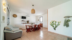 Ein Wohnzimmer mit einer Couch, einem Esstisch, Stühlen, einem Fernseher und einer Küchenzeile mit einer Uhr und Wanddekoration.