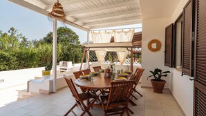 Eine überdachte Terrasse mit einem runden Tisch, Stühlen und einer hängenden Lampe.