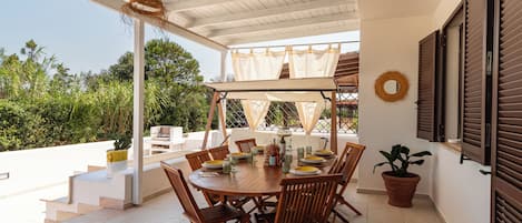 A covered patio with a round table, chairs, and a hanging light fixture.
