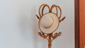 Ein Zimmer mit einem Holzhocker, einem Tisch mit Papieren und einem verzierten Hutständer.