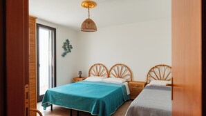 Ein Schlafzimmer mit zwei Betten, einem Korbstuhl, einem Nachttisch mit Lampe und einer Pendelleuchte.